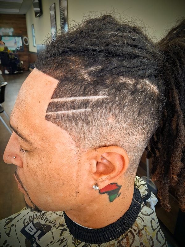 Locs pulled back with a double carved part and a low fade around the ear.